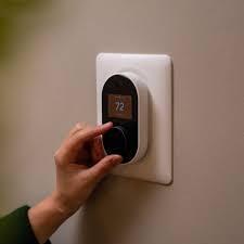 Hand adjusting Wyze Thermostat showing 72 degrees on wall
