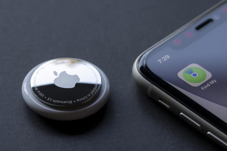 Close-up of Apple AirTag next to a smartphone on a dark surface, representing 2025 tracker comparison